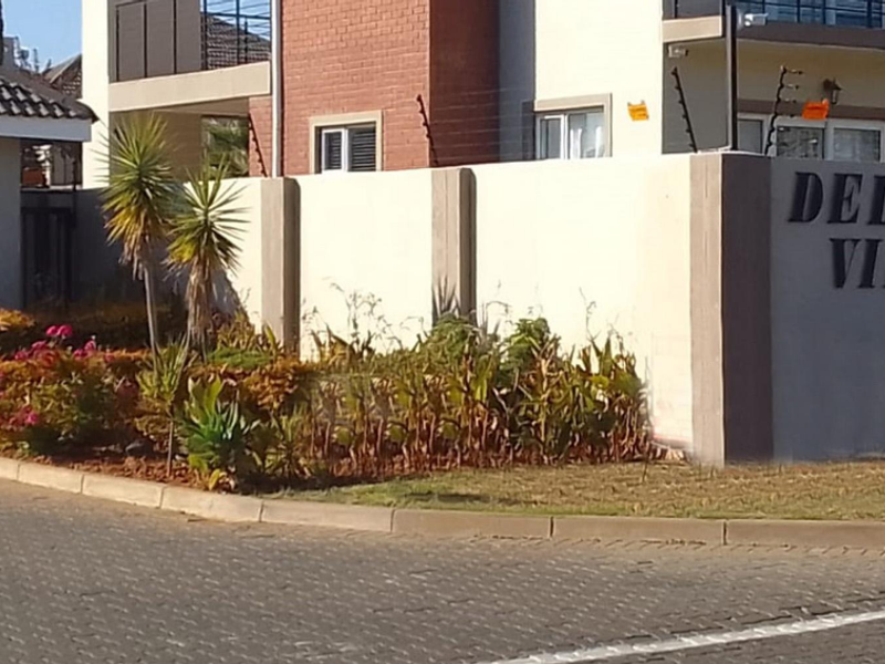Front entrance view of Delano View townhouse complex featuring a secure boundary wall, electric fencing, and established garden landscaping.