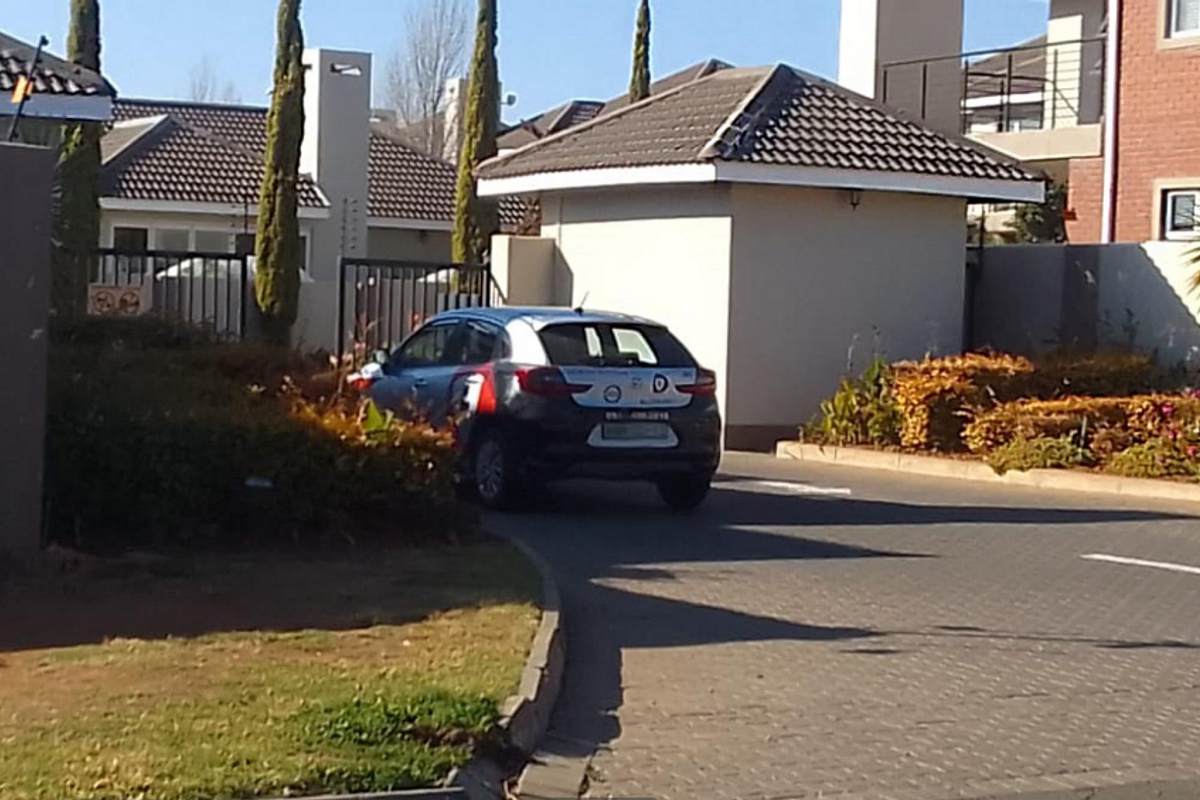 Front entrance view of the townhouse complex featuring a paved driveway, security gate, and perimeter wall with electric fencing.