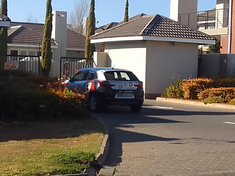 Front entrance view of the townhouse complex featuring a paved driveway, security gate, and perimeter wall with electric fencing.