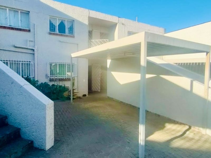Exterior view of the flat featuring a covered carport, paved driveway, and external staircase with security bars on windows.