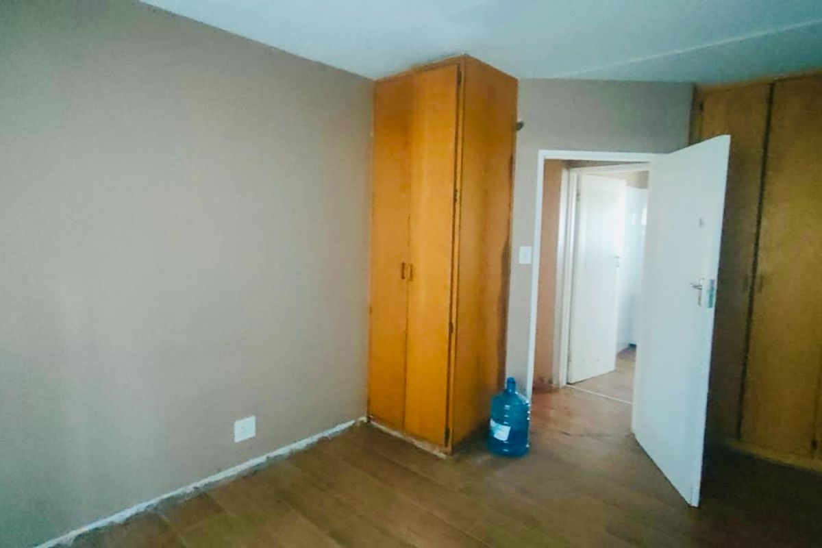 A vacant bedroom featuring built-in wooden cupboards and laminate flooring, requiring minor cosmetic updates to skirting and finishes.