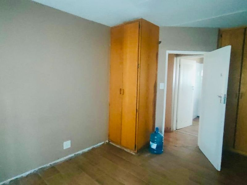 A vacant bedroom featuring built-in wooden cupboards and laminate flooring, requiring minor cosmetic updates to skirting and finishes.