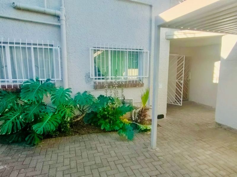 Rear exterior view of the flat featuring a paved patio area, covered walkway, and security bars on the windows.