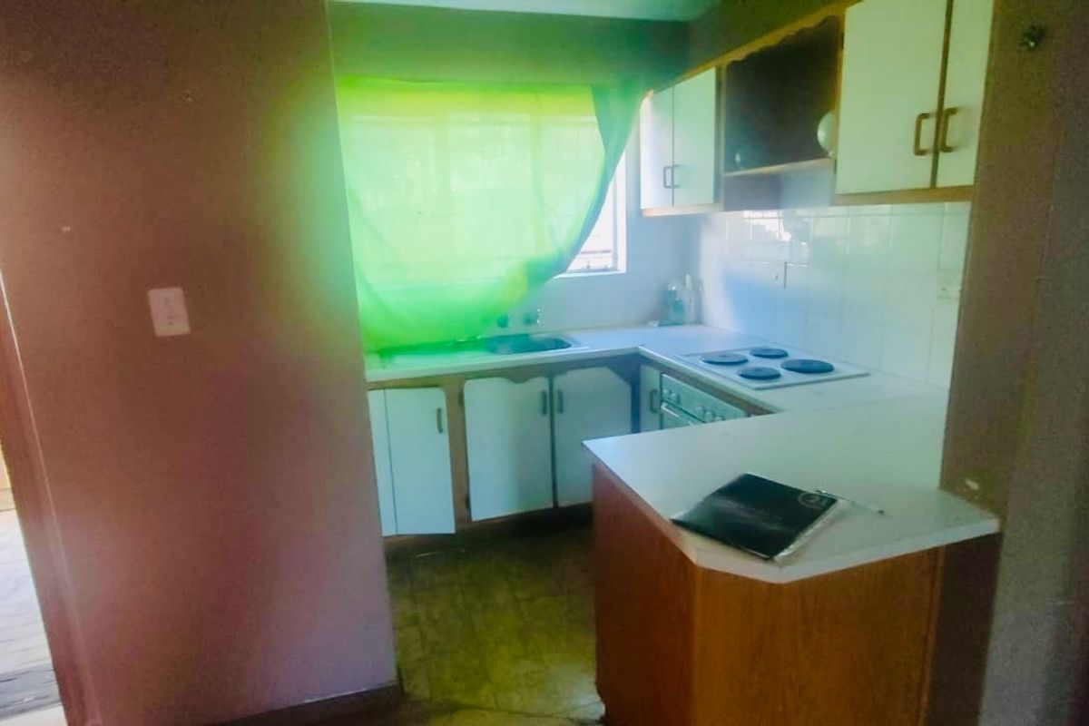 A compact kitchen featuring built-in cabinetry, an electric hob, and an oven, offering a functional layout in need of cosmetic updates.