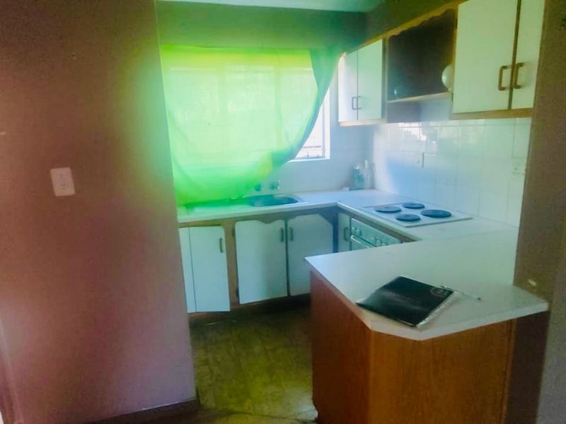 A compact kitchen featuring built-in cabinetry, an electric hob, and an oven, offering a functional layout in need of cosmetic updates.