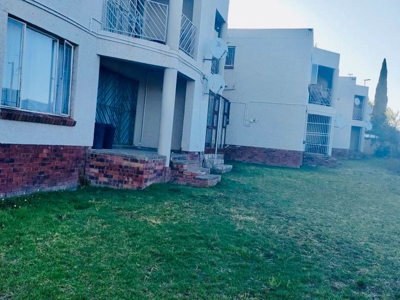 Rear view of a multi-story flat complex featuring brick base detailing, plastered walls, and private balconies with security gates.