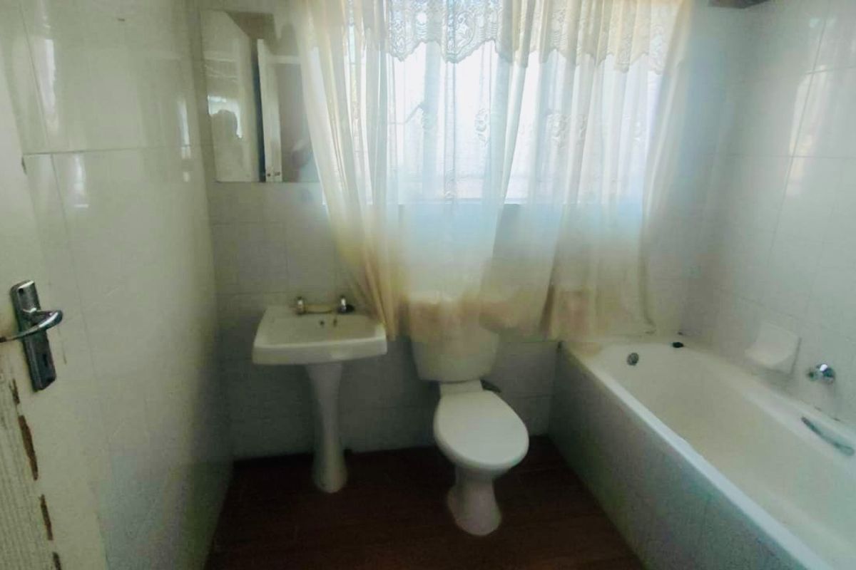 A dated bathroom featuring a pedestal basin, toilet, and bathtub with full-height wall tiling. The space requires cosmetic updates to improve its condition.