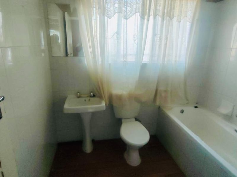 A dated bathroom featuring a pedestal basin, toilet, and bathtub with full-height wall tiling. The space requires cosmetic updates to improve its condition.