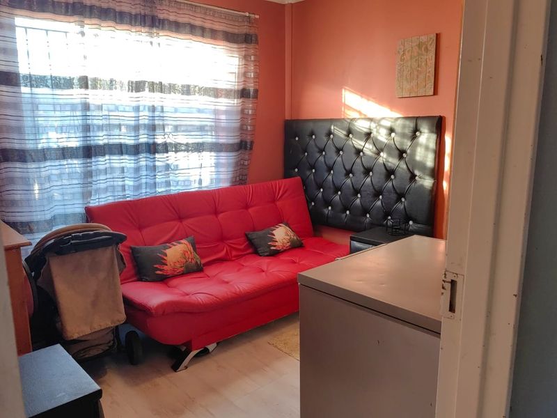 A compact bedroom featuring laminate flooring and a window fitted with security bars, currently utilized as a multi-purpose living space.