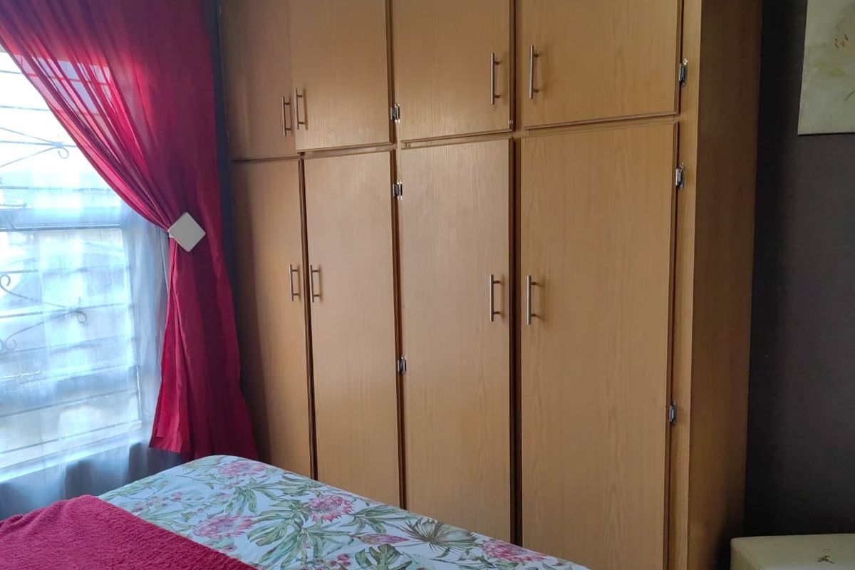 Bedroom featuring floor-to-ceiling wooden built-in cupboards and a window fitted with security bars.