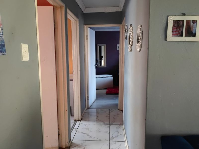 A functional hallway featuring marble-look tiled flooring and access to multiple rooms, showing signs of wear on the walls and door frames.