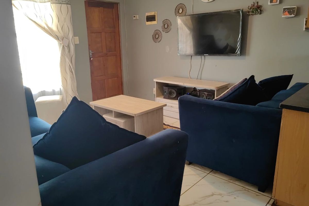 A living room area featuring tiled flooring and a wooden door, providing a functional space for relaxation.