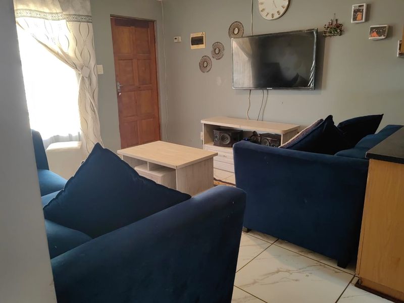 A living room area featuring tiled flooring and a wooden door, providing a functional space for relaxation.