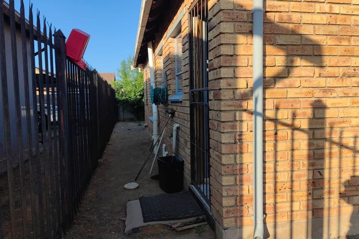 A narrow side passage of the property featuring brick exterior walls, security gate, and metal perimeter fencing.