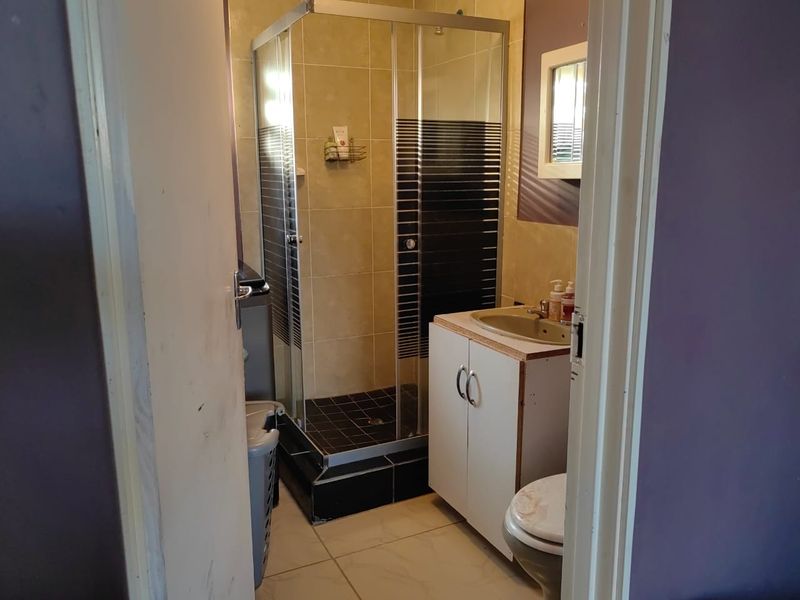 A compact bathroom featuring a shower enclosure, vanity cabinet with basin, and toilet, finished with tiled walls and flooring.