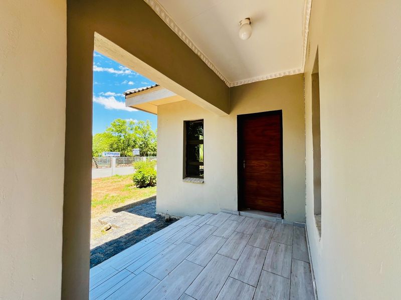 A clean and well-maintained covered entrance porch featuring modern wood-look floor tiles and a solid wooden front door.