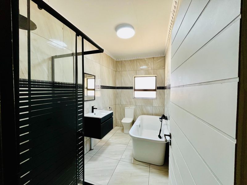 Modern bathroom featuring a freestanding bathtub, walk-in shower with black frame, wall-mounted vanity, and neutral floor-to-ceiling tiling.