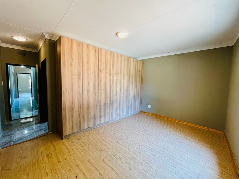 A clean, empty bedroom featuring modern wood-look laminate flooring and extensive built-in cupboards with a light wood finish.