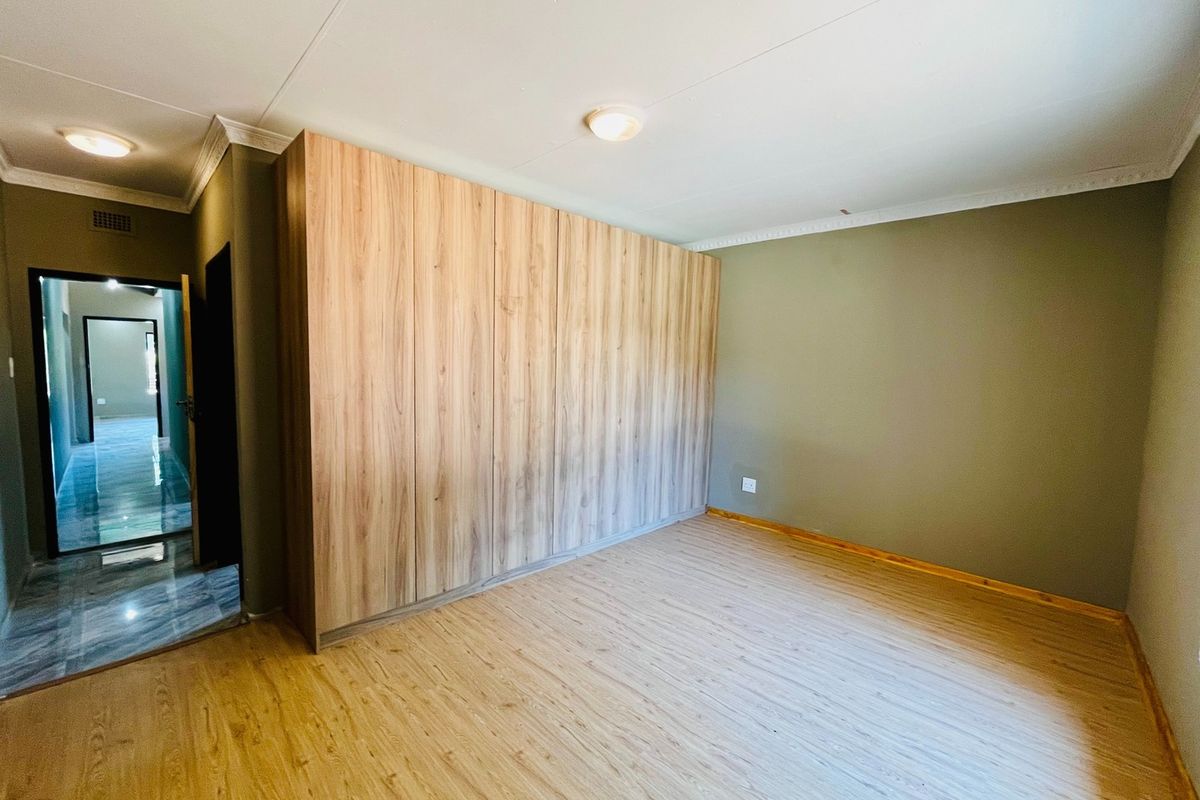 A clean, empty bedroom featuring modern wood-look laminate flooring and extensive built-in cupboards with a light wood finish.