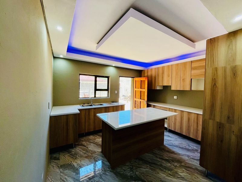 Modern kitchen featuring wood-finish cabinetry, a central island with stone countertops, tiled flooring, and a contemporary drop ceiling with integrated LED lighting.