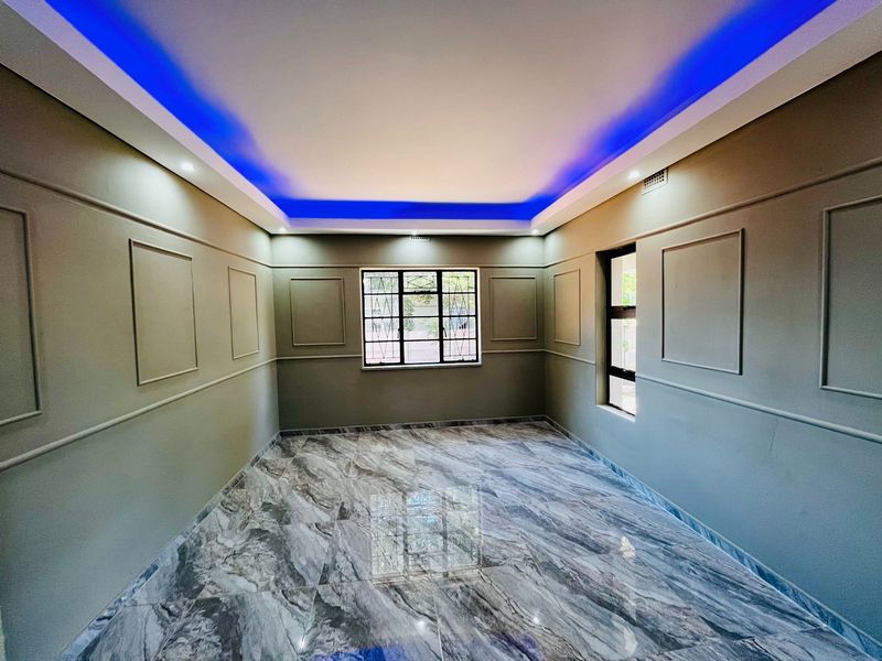A bright, empty living room featuring modern marble-look floor tiles, decorative wall paneling, and a recessed ceiling with integrated blue LED accent lighting.