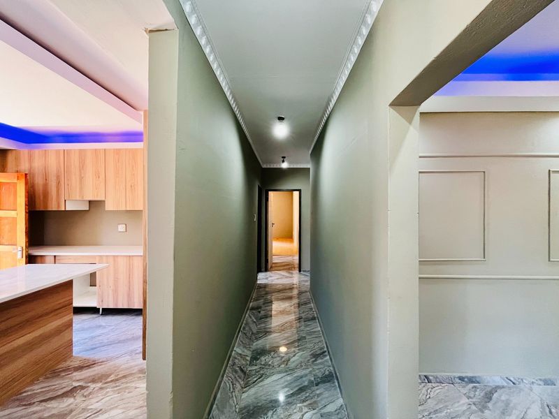 A bright, modern hallway featuring polished marble-look floor tiles, decorative cove molding, and wainscoting, leading into an open-plan kitchen area.