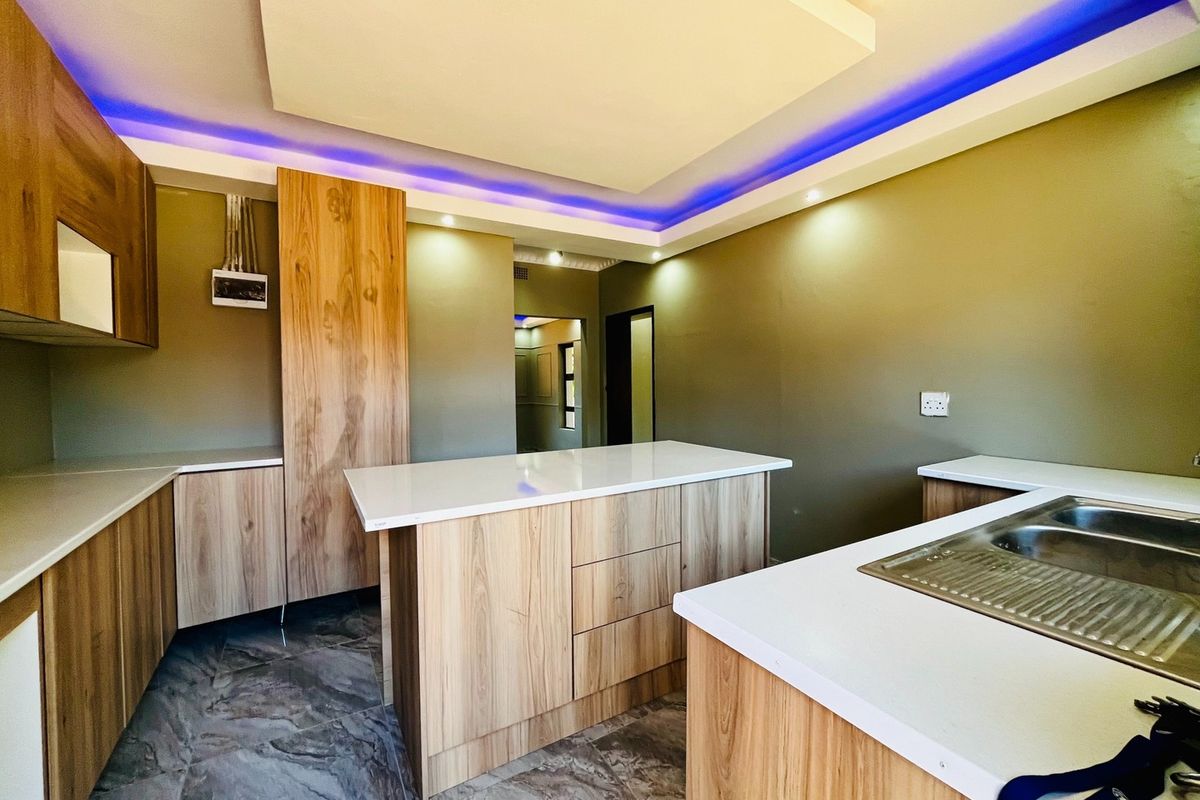 Modern kitchen featuring light wood cabinetry, stone countertops, a central island, and contemporary recessed ceiling lighting with integrated LED accents.