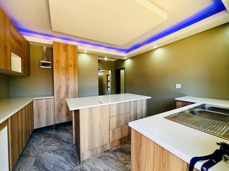 Modern kitchen featuring light wood cabinetry, stone countertops, a central island, and contemporary recessed ceiling lighting with integrated LED accents.