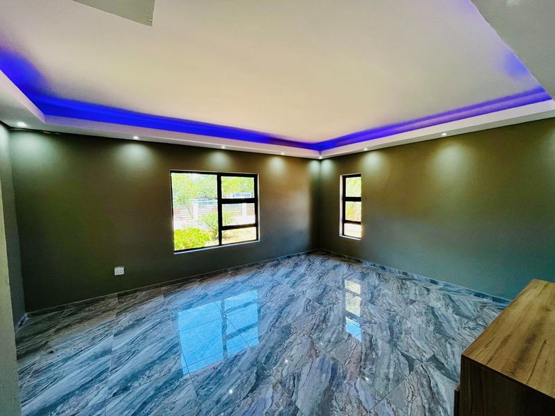 Spacious living area featuring polished marble-effect floor tiles, recessed ceiling lighting with blue LED cove accents, and modern aluminium-framed windows.