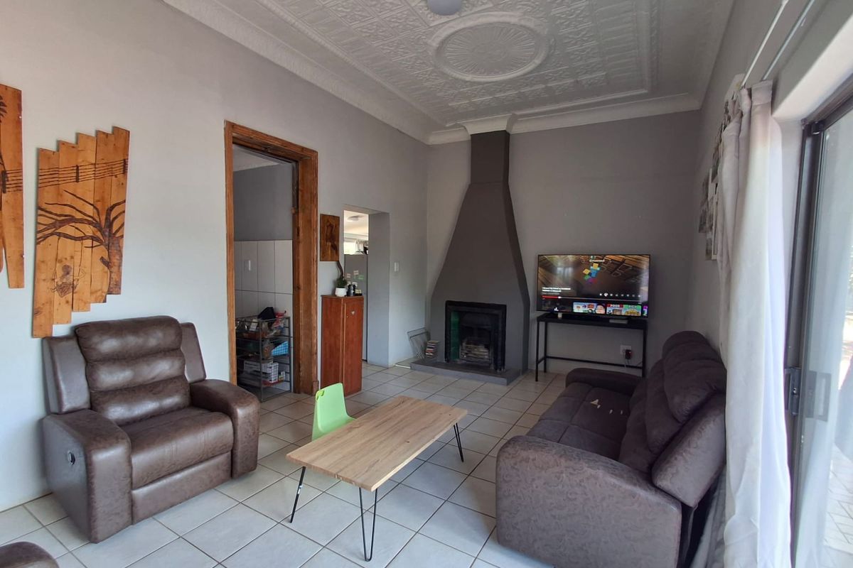 A living room featuring a central fireplace, decorative ceiling detailing, and tiled flooring, with direct access to an outdoor area via a sliding glass door.