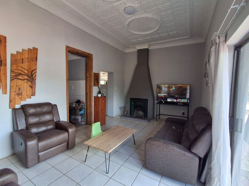A living room featuring a central fireplace, decorative ceiling detailing, and tiled flooring, with direct access to an outdoor area via a sliding glass door.