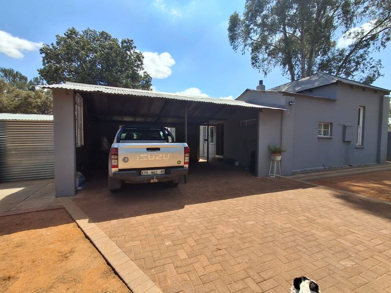 Front exterior view of the property featuring a paved driveway, a covered carport area, and a well-maintained masonry building facade.