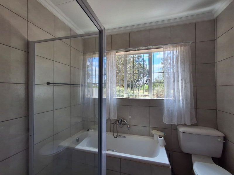 A functional bathroom featuring a built-in bathtub, a separate glass-enclosed shower, and neutral ceramic wall tiling with natural light from the window.