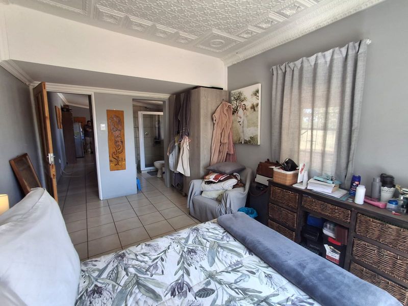 A bedroom featuring tiled flooring, a decorative pressed metal ceiling, and an en-suite bathroom, offering a functional layout with built-in storage.
