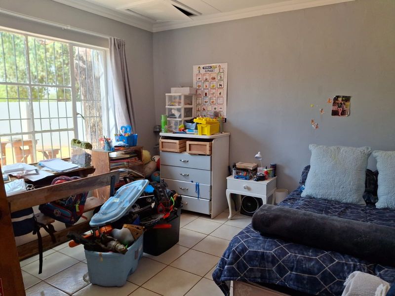 A bedroom featuring tiled flooring, security bars on the window, and ceiling cornice detail. The room requires minor ceiling repairs.
