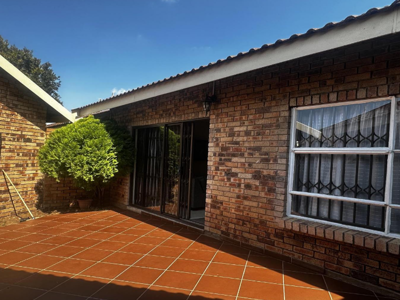 A well-maintained rear exterior view of a townhouse featuring a paved patio, face brick walls, and secure sliding door access.