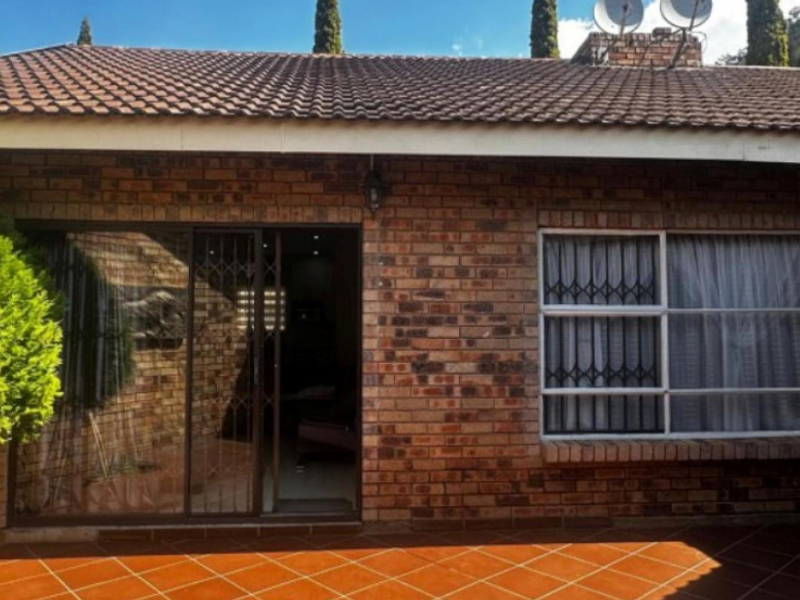 Rear exterior view of the townhouse featuring a face brick facade, tiled patio area, and secure sliding door access.