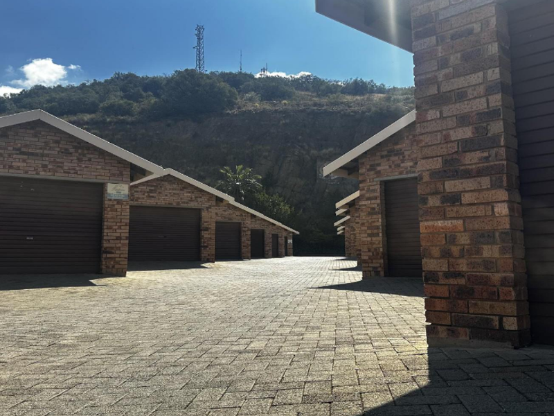 A row of brick-faced garages with roller shutter doors and a paved driveway, set against a hillside backdrop.