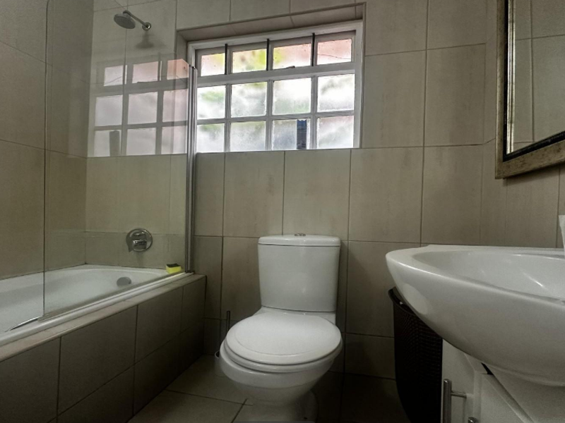 A functional bathroom featuring a bathtub with a glass shower screen, a toilet, and a vanity basin with tiled finishes throughout.