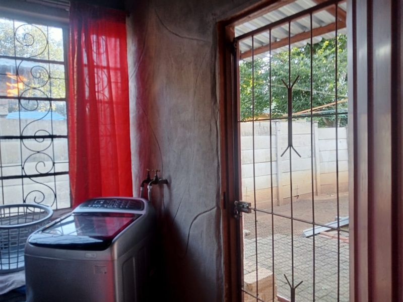 A functional laundry area featuring a security gate, exterior access, and exposed textured wall finishes.