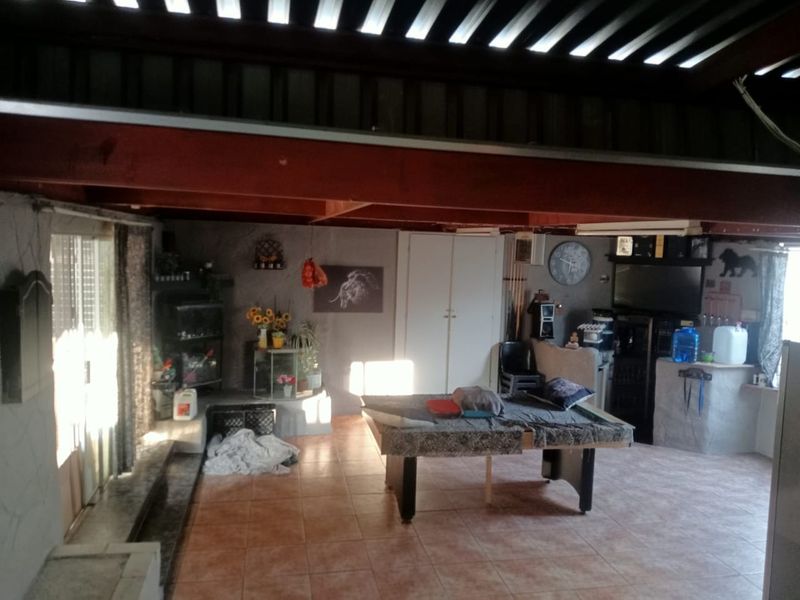 Spacious covered patio area featuring tiled flooring, exposed timber beams, and a built-in bar counter, offering a versatile space for outdoor entertainment.