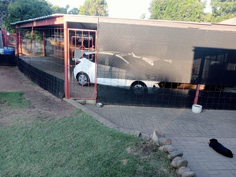 A functional carport structure featuring a metal frame, shade cloth covering, and wire mesh fencing, situated over a paved driveway area.