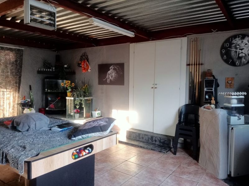 A multi-purpose garage space featuring exposed steel roof beams, tiled flooring, and built-in storage cupboards, currently utilized as a recreational area.