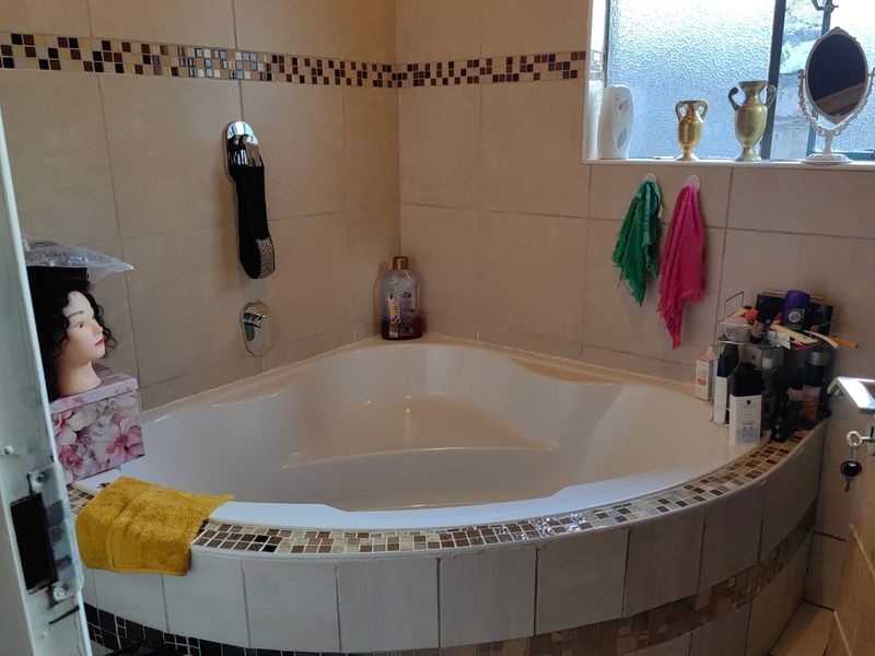 A bathroom featuring a corner bathtub with tiled surround and a decorative mosaic border, complemented by an obscured glass window for privacy.