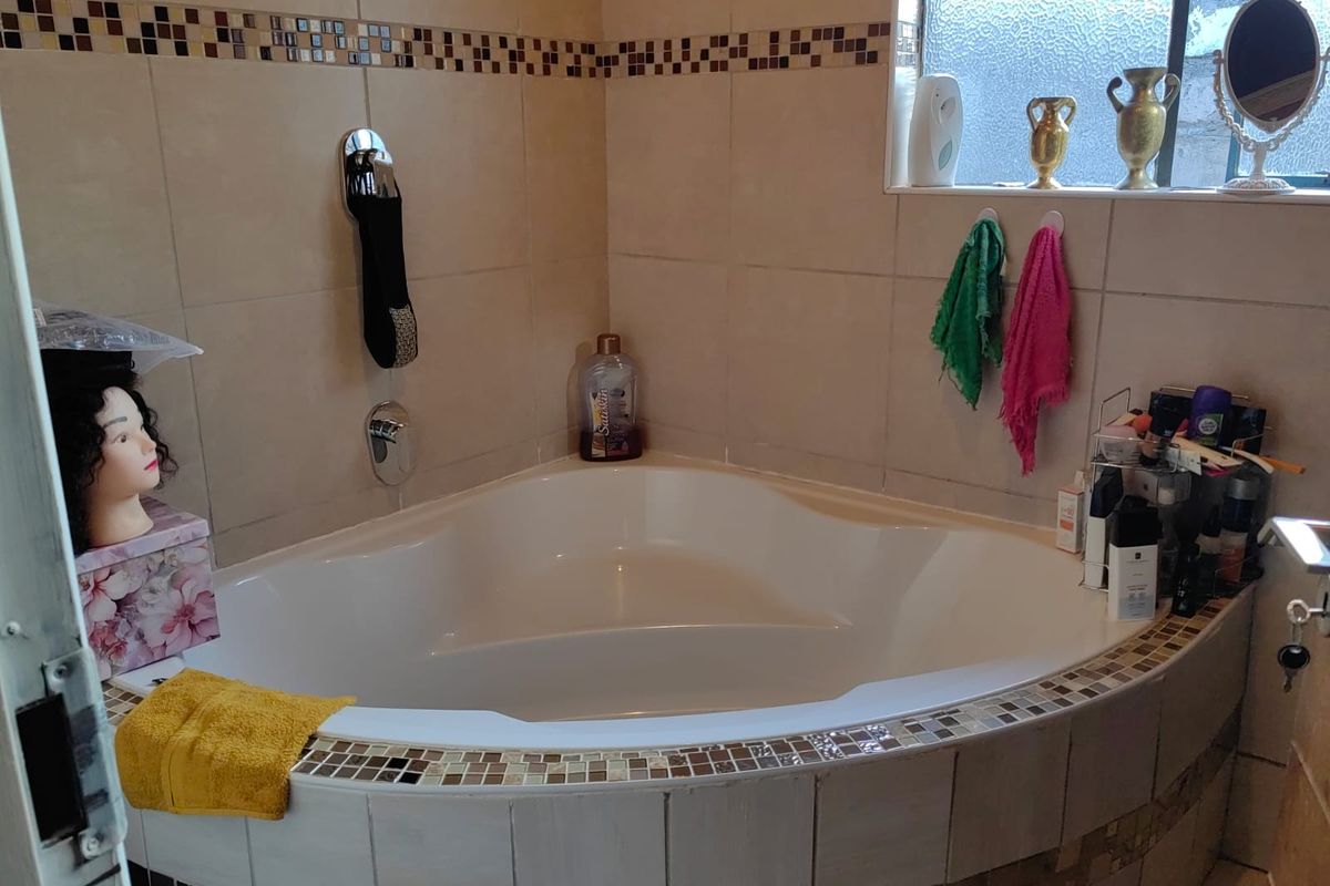 A bathroom featuring a corner bathtub with tiled surround and a decorative mosaic border, complemented by an obscured glass window for privacy.