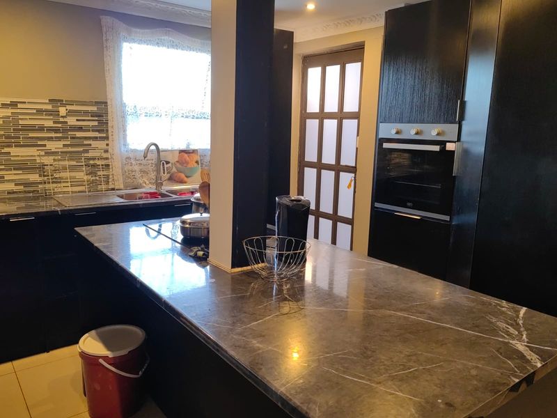 A functional kitchen featuring dark cabinetry, a stone-topped island, built-in oven, and a mosaic tile backsplash with ample counter space.