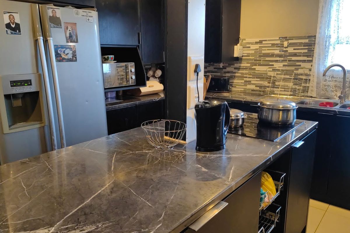 A functional kitchen featuring dark cabinetry, a marble-look countertop, mosaic tile backsplash, and a built-in induction hob with a stainless steel sink.