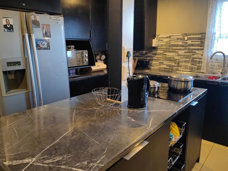 A functional kitchen featuring dark cabinetry, a marble-look countertop, mosaic tile backsplash, and a built-in induction hob with a stainless steel sink.