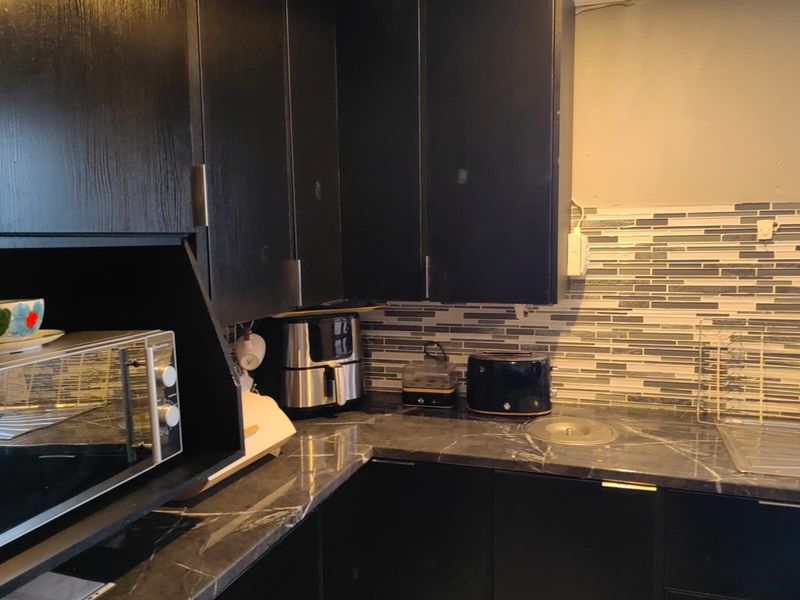 A compact kitchen area featuring dark cabinetry, a marble-effect countertop, and a modern mosaic tile backsplash.