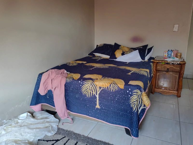A bedroom featuring tiled flooring and plain walls, currently showing signs of wear and surface damage requiring maintenance.